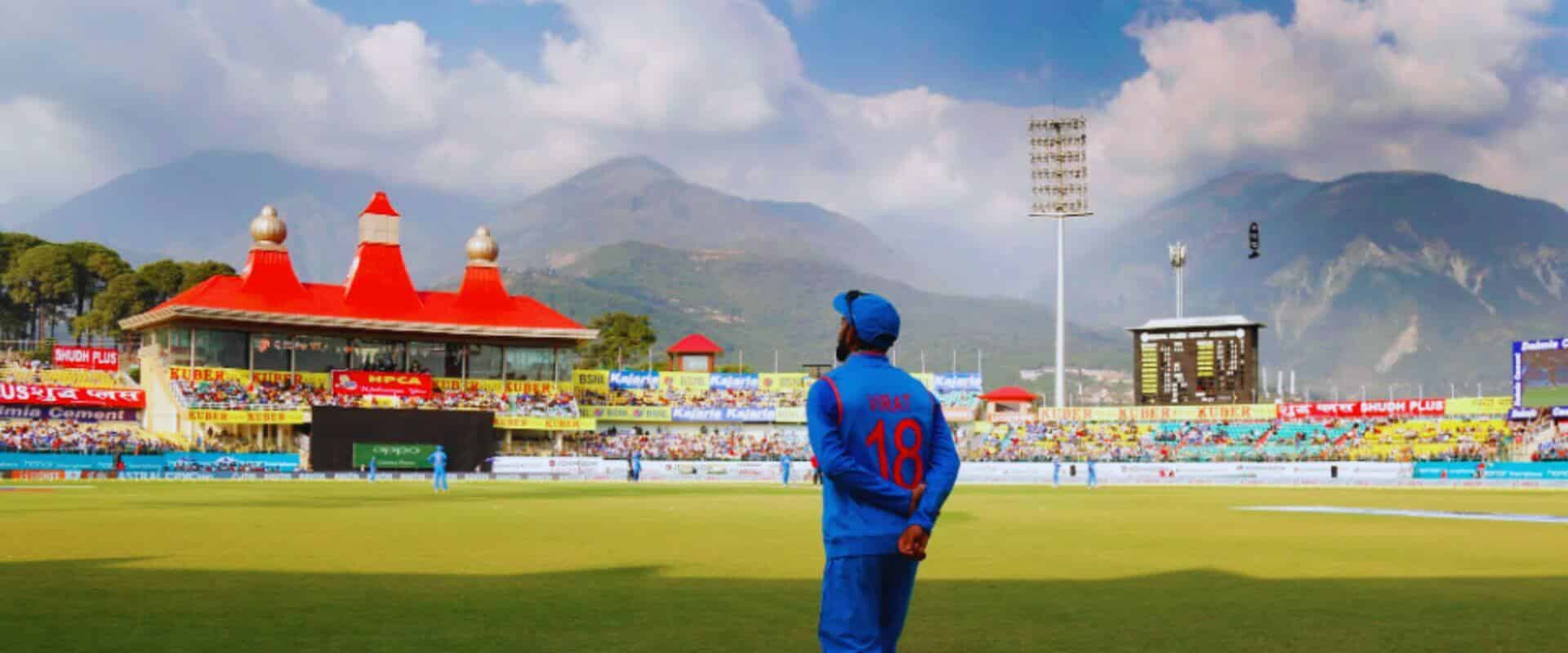 Stunning aerial view of the Himachal Pradesh Cricket Association Stadium, Dharamshala with the majestic Dhauladhar mountains in the background — a world-renowned cricket venue surrounded by Himalayan beauty.